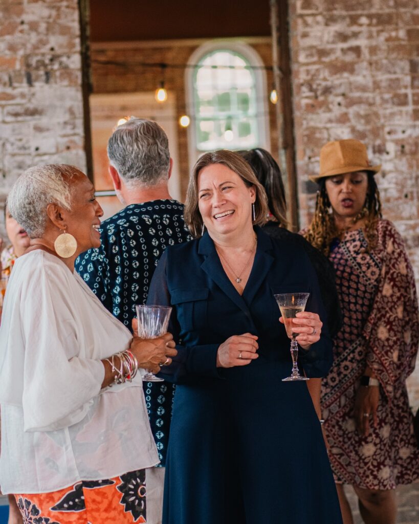 Nina Williams-Mbengue laughing during conversation with Amanda Brandes holding a drink.