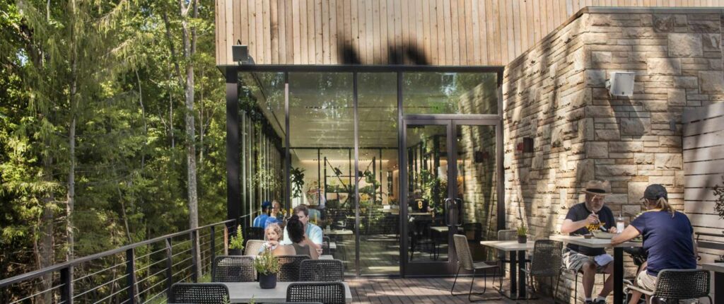 People dining on a sunny outdoor patio at a restaurant with wood and stone architecture.