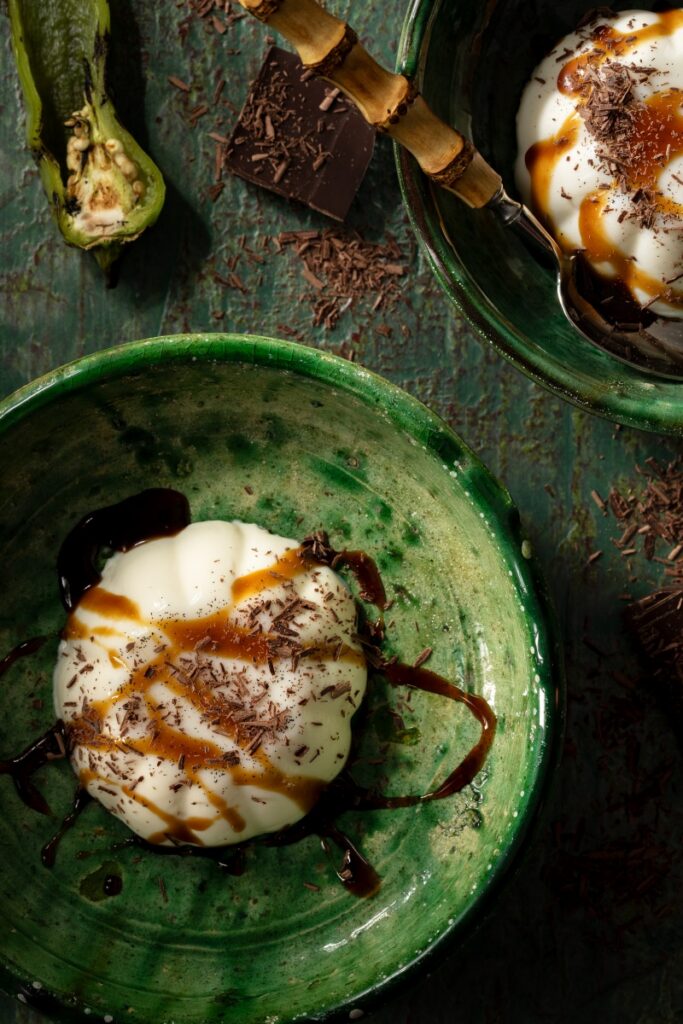Vanilla bean panna cotta topped with espresso green chile caramel drizzle and shaved chocolate in a green bowl.