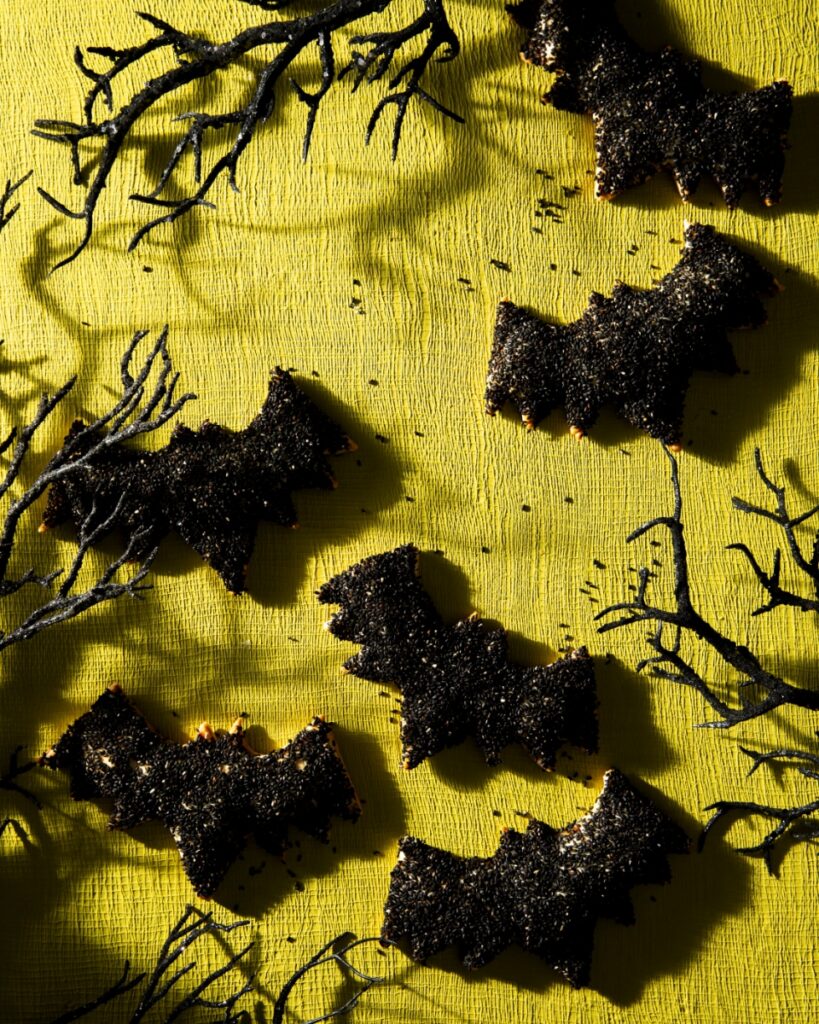 Bat-shaped hand pies coated in black sesame seeds on a platter for a Halloween party.