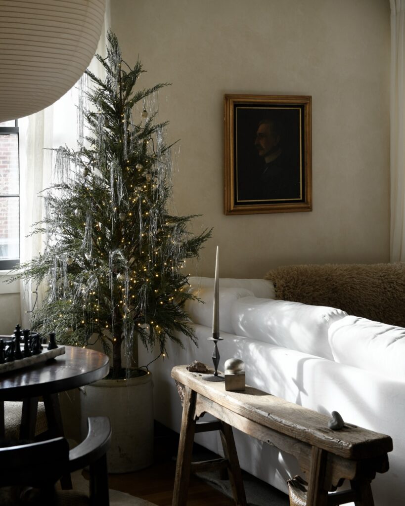 Foraged holiday decor: A natural Christmas tree with lights and tinsel in a cozy living room.