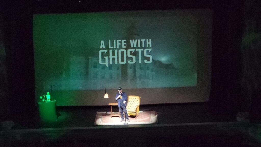 Man on stage with "A Life With Ghosts" backdrop, Pittsburgh paranormal event