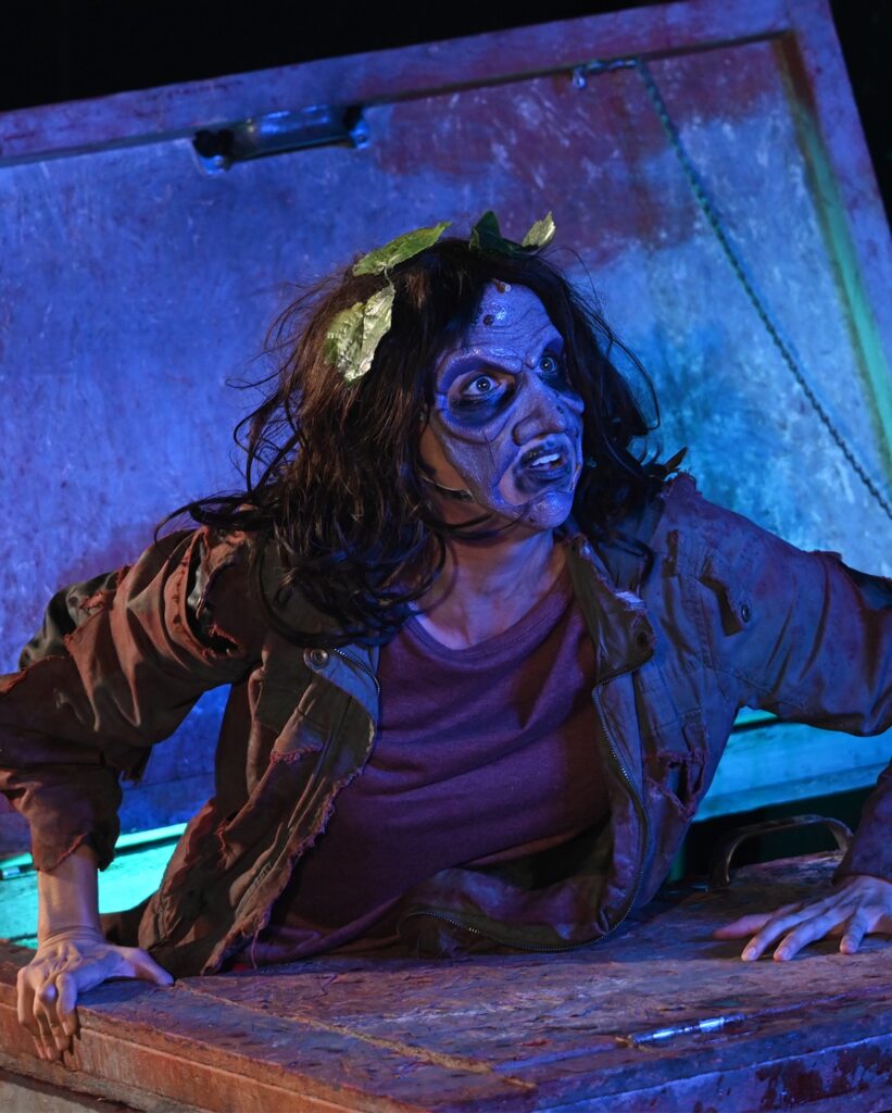 Zombie actor emerging from a coffin in a Halloween musical performance.