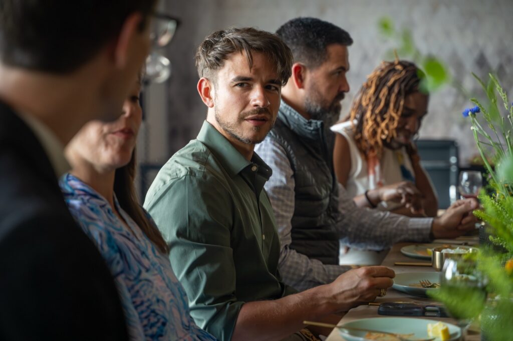 Diverse group at a dinner table, with a man in a green shirt looking at the camera.