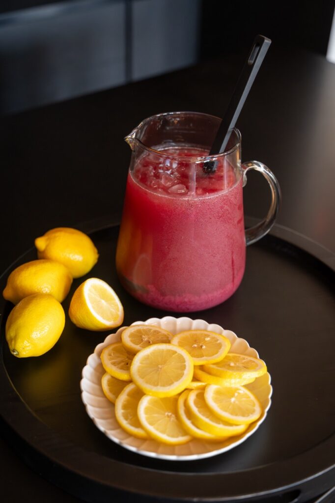 Pitcher of pink lemonade with sliced lemons on a tray