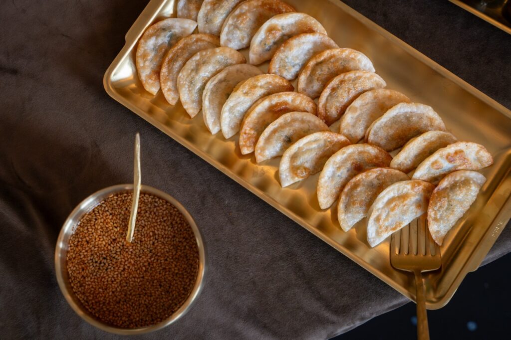 Golden pan-fried dumplings served on a brass tray with sesame seeds