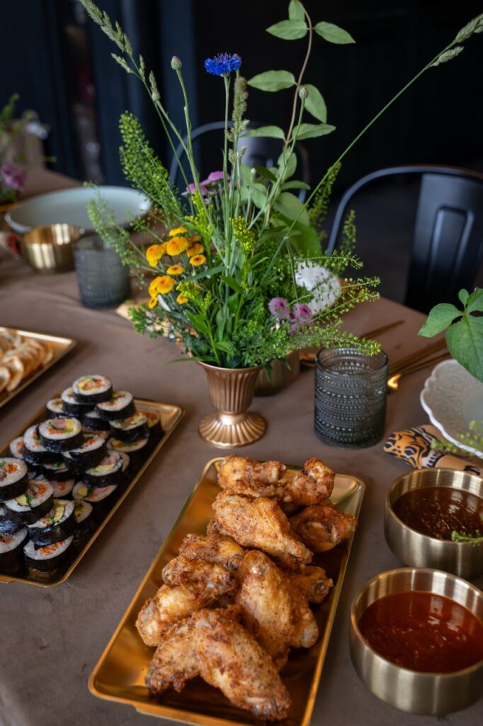Platter of chicken wings and sushi rolls on a table with a floral centerpiece