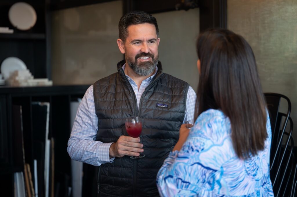 Man in Patagonia vest holding drink, talking to woman in Pittsburgh