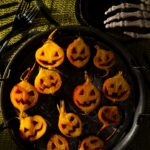 A tray of roasted golden beet halves carved with jack o’lantern faces and drizzled with apple cider glaze on a platter.