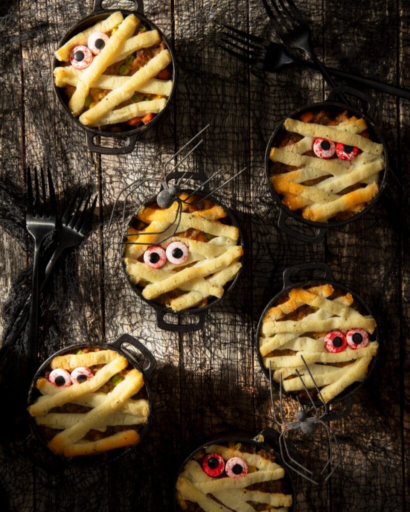 Individual mini cast-iron crocks filled with Shepherd's pie and topped with piped mashed potato mummy wraps and candy eyeballs.