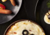 Halloween Mummy Dip: A Baked Pizza Dip Wrapped in String-Cheese Bandages A round bowl of pizza dip with strips of white cheese over top and two olives to look like a mummy.