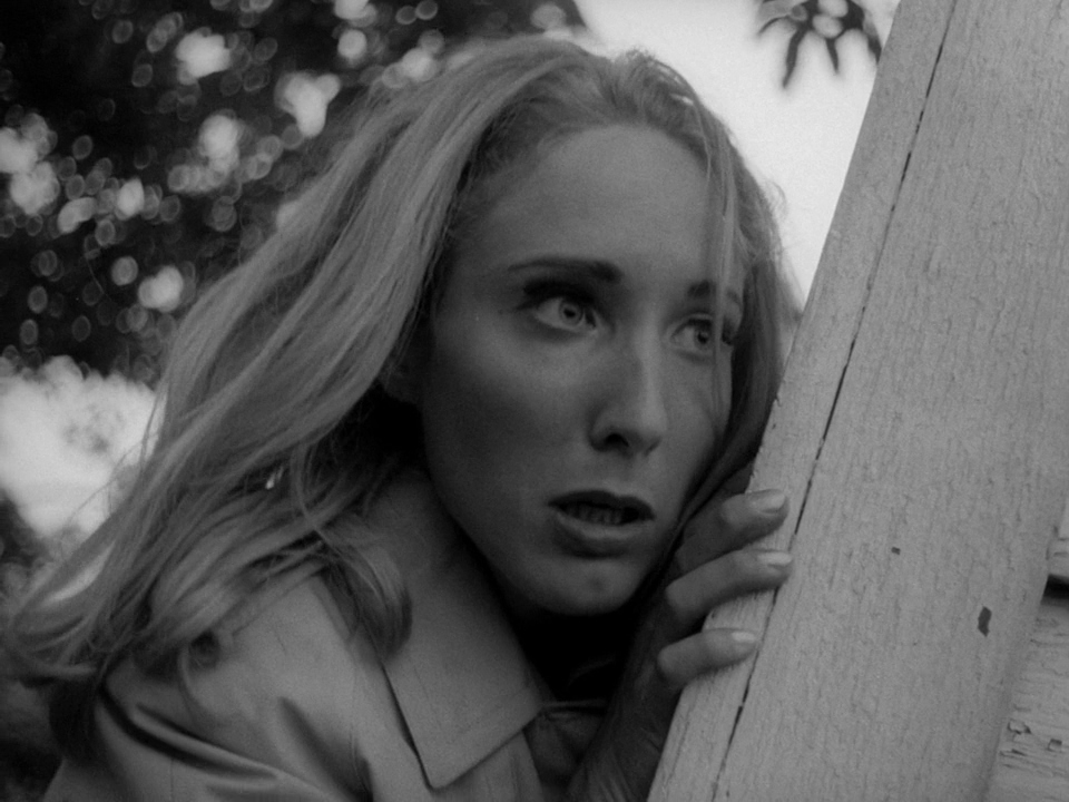 Scared blonde woman peeking around wooden post in black and white horror scene