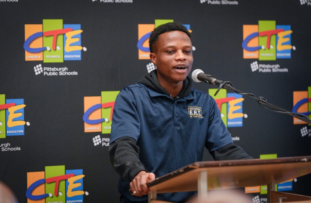 Young man speaking at a podium with CTE Pittsburgh Public Schools backdrop