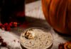 Pumpkin Spice Martini Recipe: A Fall Cocktail That’s Hauntingly Good A pumpkin spice martini on a table with a marshmallow garnish sitting beside a pumpkin and bottle of red infused liquor.