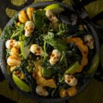 A serving bowl of roasted squash salad with kale, apple, and pepitas, topped with mozzarella skulls for Halloween.