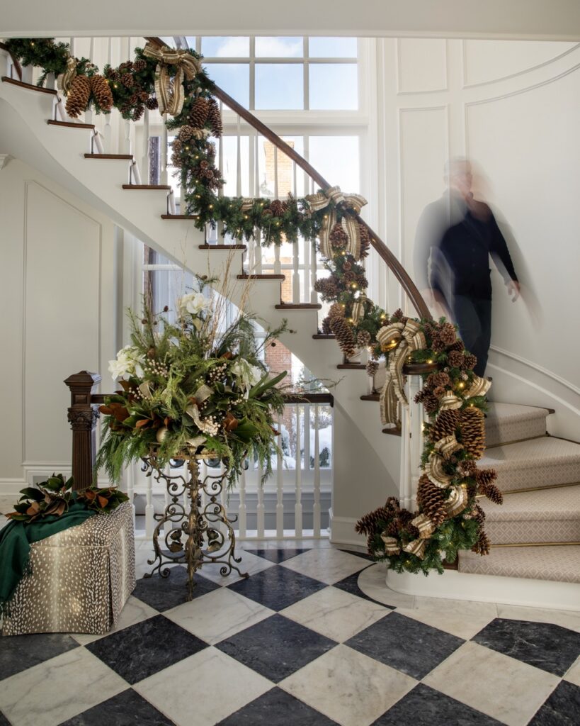 Luxurious holiday home staircase decorated with pinecones, garlands, and floral arrangements.