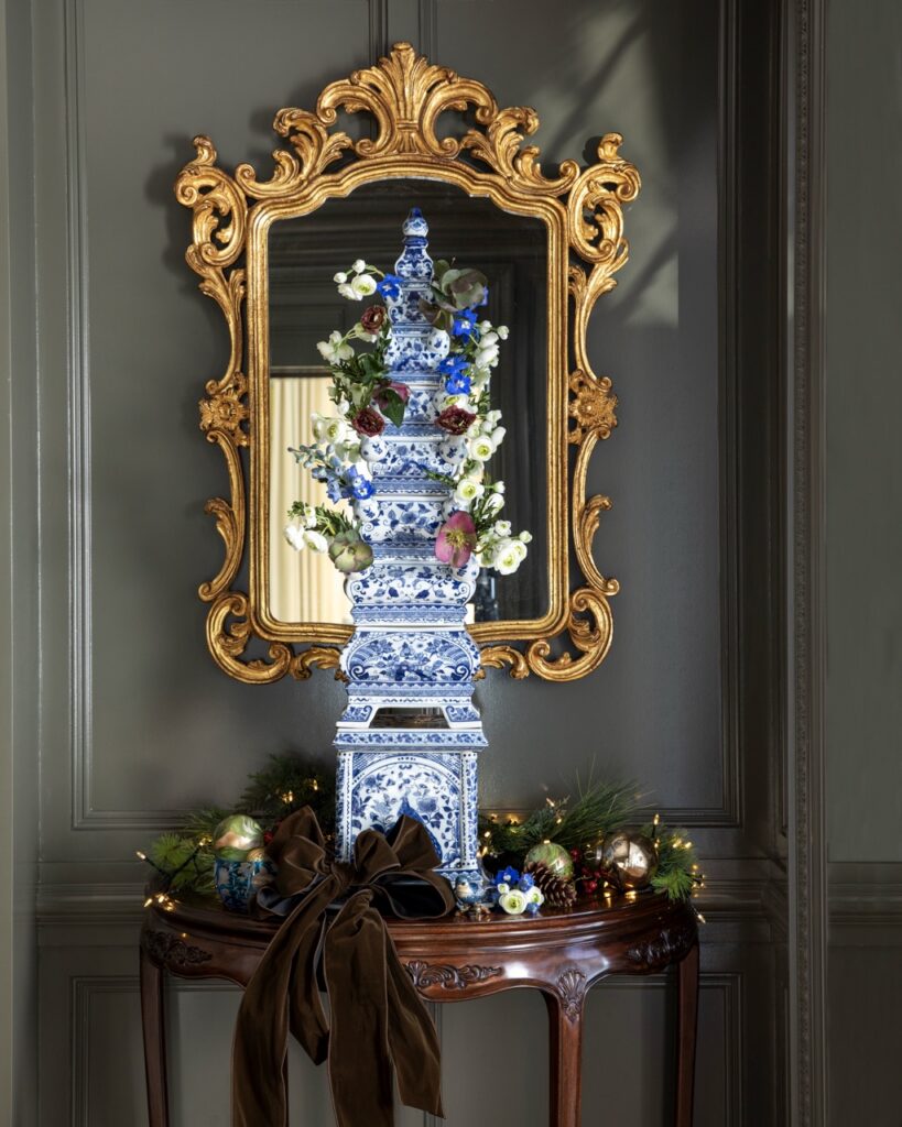 Luxurious holiday decor: Blue & white porcelain tower with floral arrangement & festive garland.
