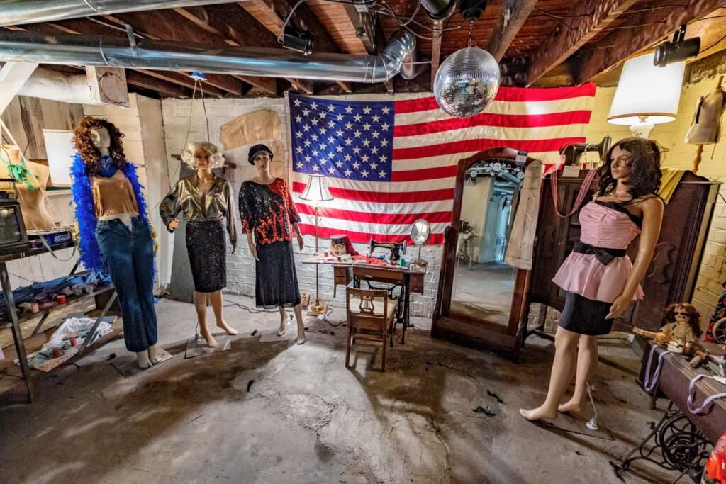 Mannequins in vintage clothing stand before an American flag in a room with a sewing machine.