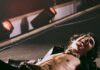 Sombr at PPG Paints Arena: What to Know Before You Go Sombr laying on the stage at a concert with an open black jacket, leather pants, and his tongue out.
