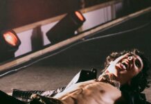 Sombr at PPG Paints Arena: What to Know Before You Go Sombr laying on the stage at a concert with an open black jacket, leather pants, and his tongue out.