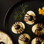 Deviled eggs topped with black olive spiders on a Halloween serving platter.