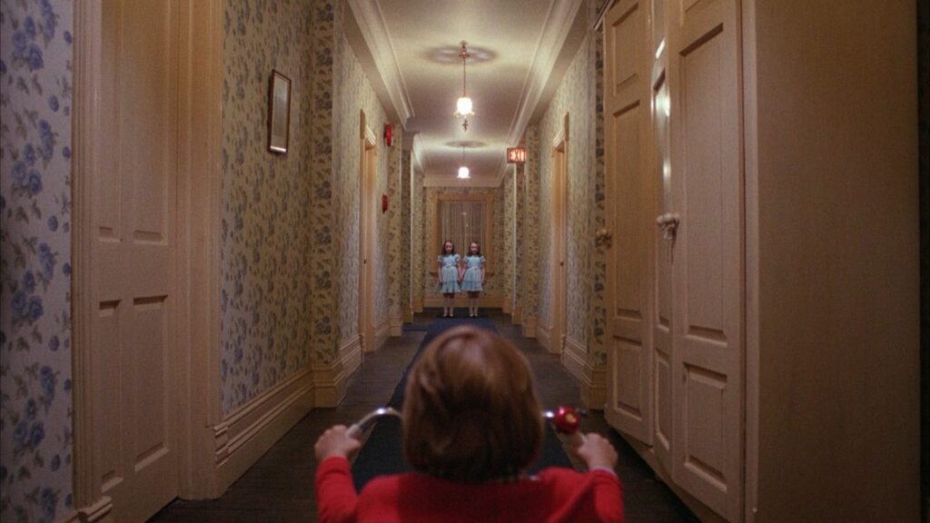 Danny Torrance rides his tricycle down a creepy hotel hallway towards twin ghost girls.